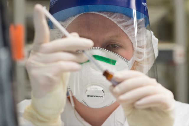 Veterinarian wearing a face shield and mask measuring medication from a bottle.