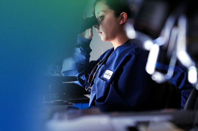 Research technician wearing Charles River lab coat looking through microscope during a stage of small molecule drug development 