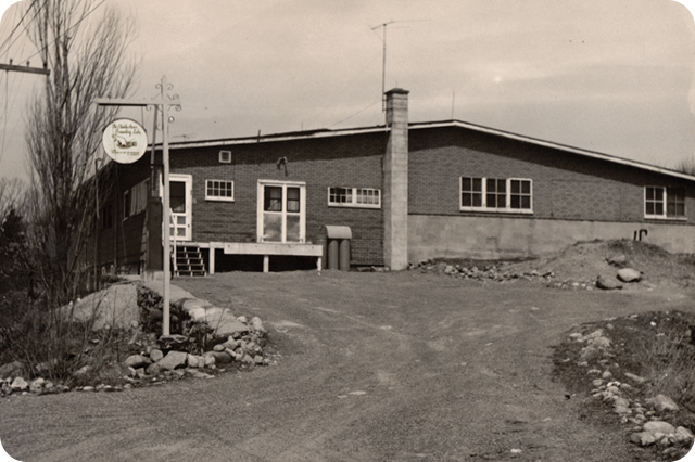 Historic photo of a Charles River Laboratories facility, showing an early building surrounded by a gravel driveway and natural landscape.