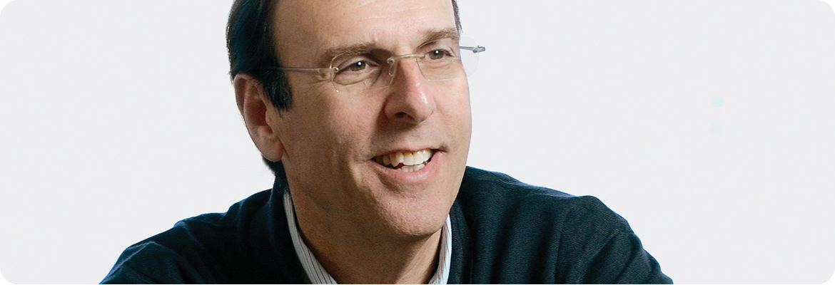 Jim Foster smiling, wearing glasses and a dark sweater, with a neutral background