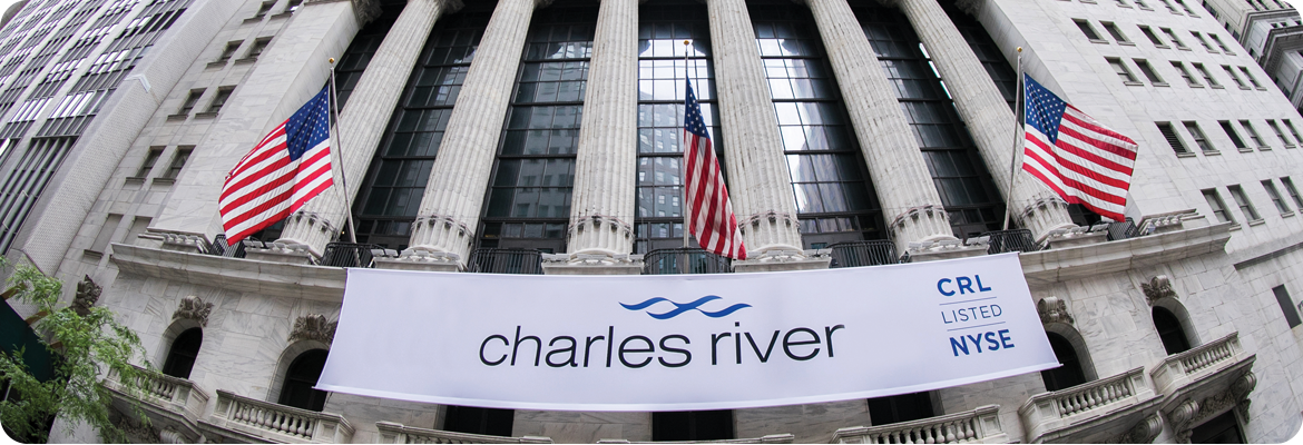 The front of the New York Stock Exchange building, adorned with large American flags and a prominent banner that reads Charles River with the text CRL Listed NYSE to the side.