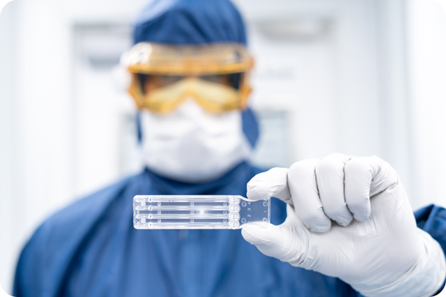 Scientist in full protective gear holding a transparent lab slide, focusing on the slide with blurred background.